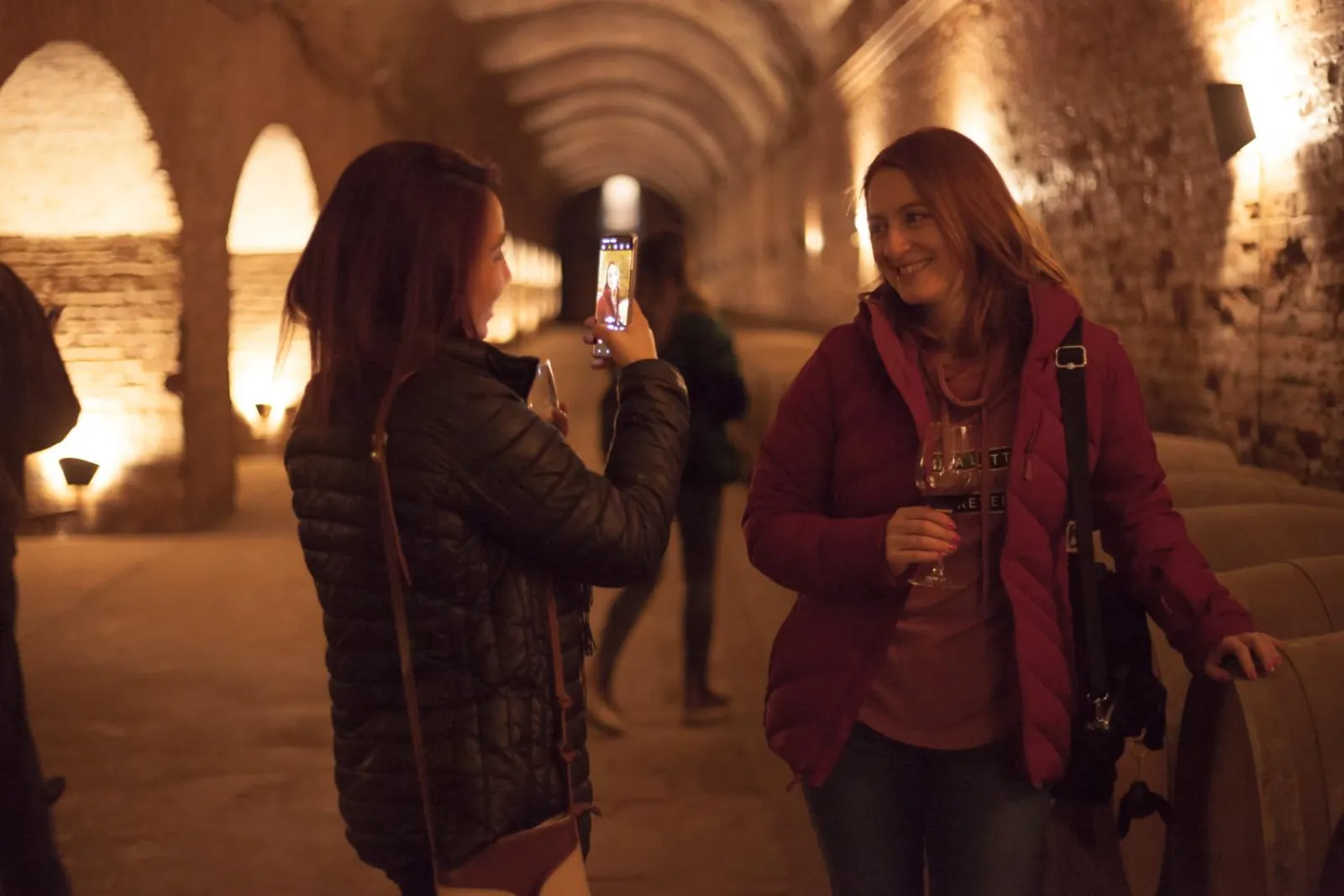 Smiling guest with wine posing for a phone photo in an arched cellar