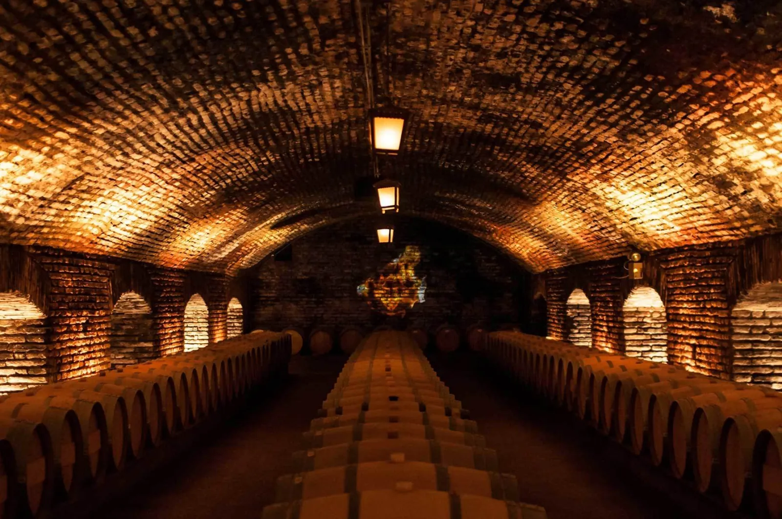 Lantern-lit brick vaulted cellar with three long rows of oak barrels