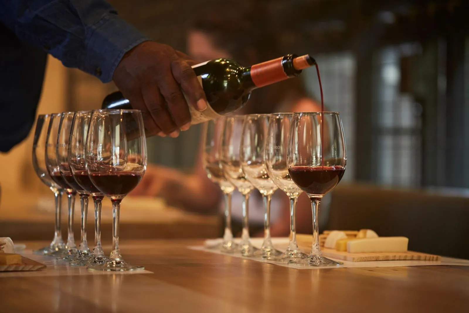 Red wine poured into a row of tasting glasses beside cheese