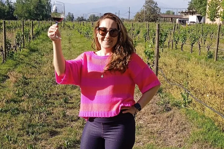 Woman raising a glass of red wine between green vineyard rows