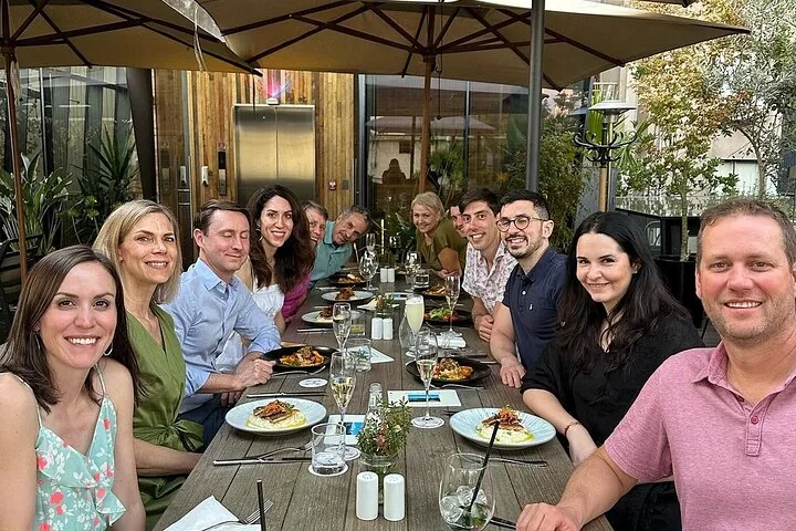 Large group lunching at a long table under restaurant umbrellas