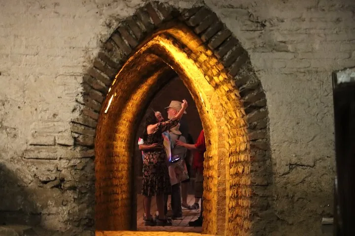 Visitors seen through a glowing pointed brick archway in an old cellar