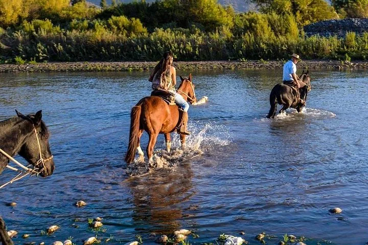 Two riders splashing across a shallow river in evening light