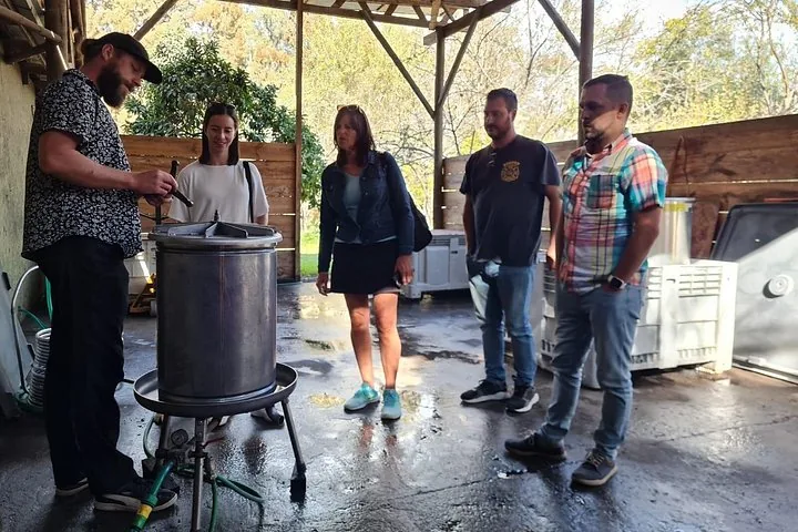 Winemaker showing a steel press to visitors under an open-sided shed