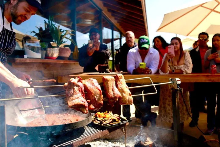 Cook roasting large cuts of meat over a fire while diners take photos