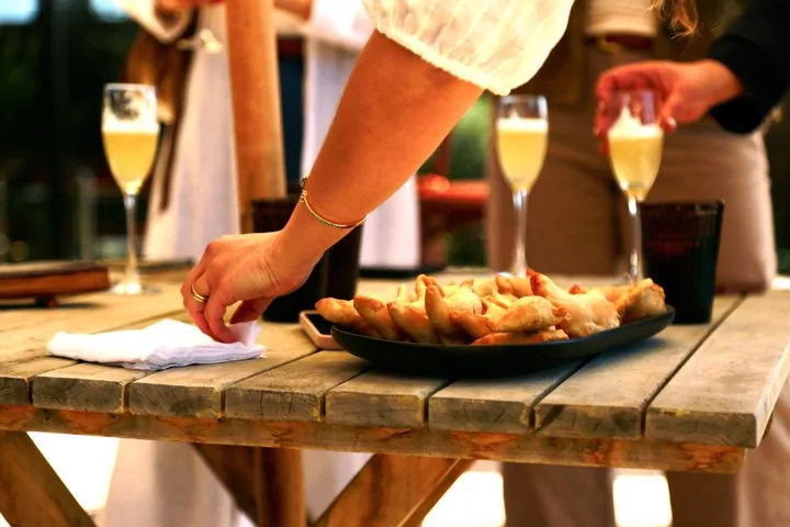 Platter of golden empanadas on a wooden table with sparkling drinks