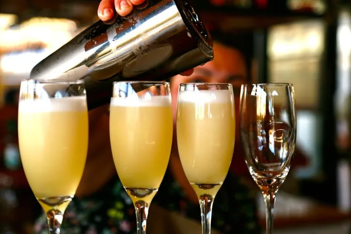 Pisco sours poured from a shaker into three tall glasses