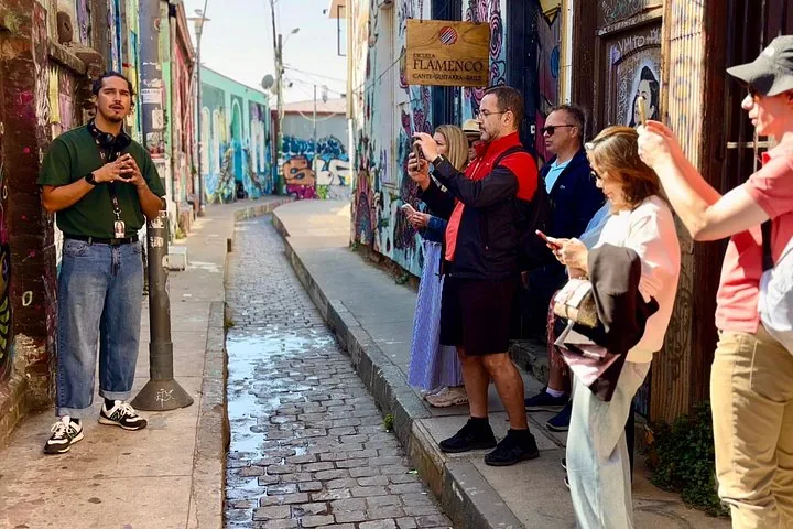 Guide speaking to a group on a cobbled lane lined with murals