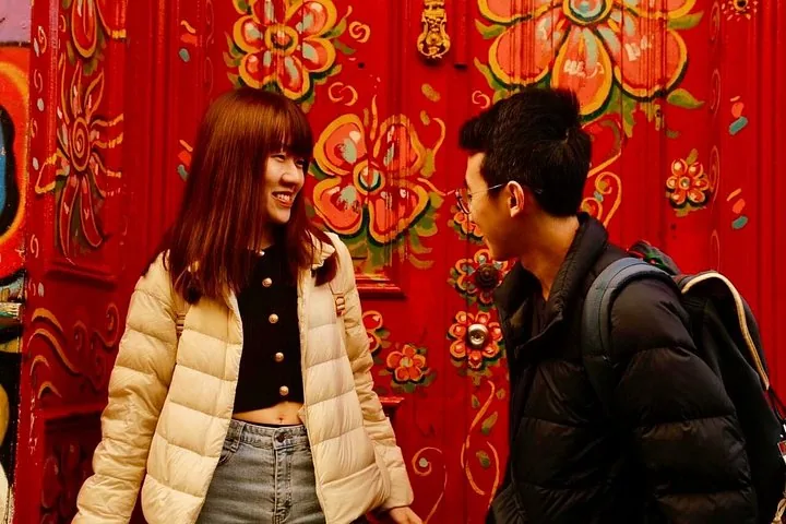 Two travelers chatting in front of a red door painted with flowers