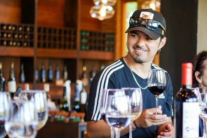 Smiling visitor with a glass of red wine in a bottle-lined tasting room