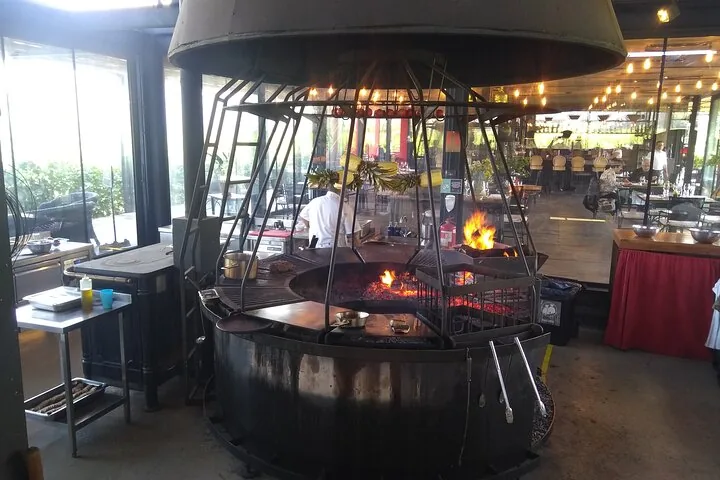 Large circular fire grill with flames under a metal dome in a restaurant