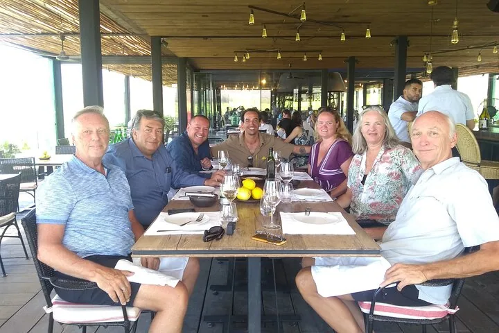 Seven diners at a set table on a shaded restaurant terrace