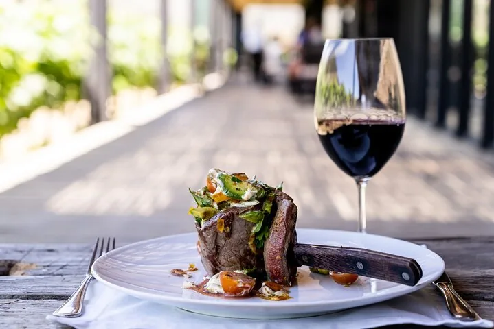 Grilled steak topped with salad on a white plate beside red wine