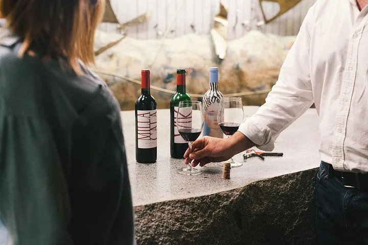 Host pouring red wine beside Milla Cala, VIK and La Piu Belle bottles
