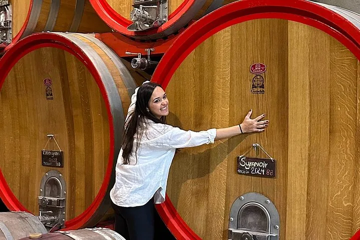 Visitor hugging a giant oak cask with red rims and chalkboard labels