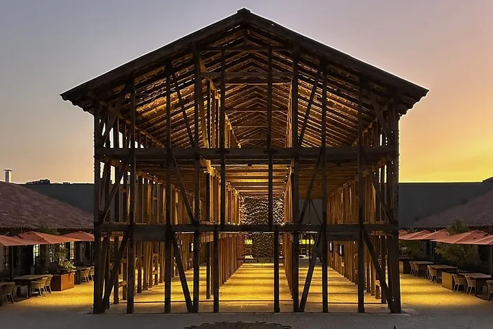 Open timber-frame pavilion at dusk between outdoor dining terraces
