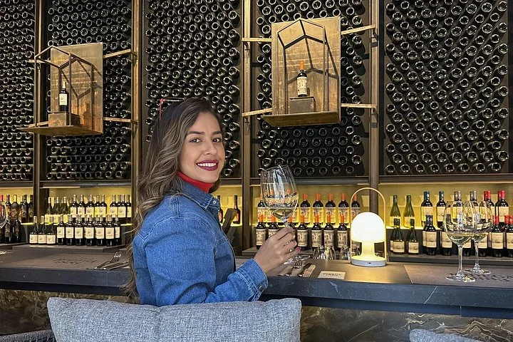 Guest holding a wine glass at a bar backed by bottle walls