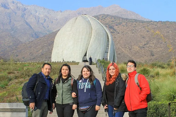 Five visitors posing below the white Bahá'í temple and dry mountains