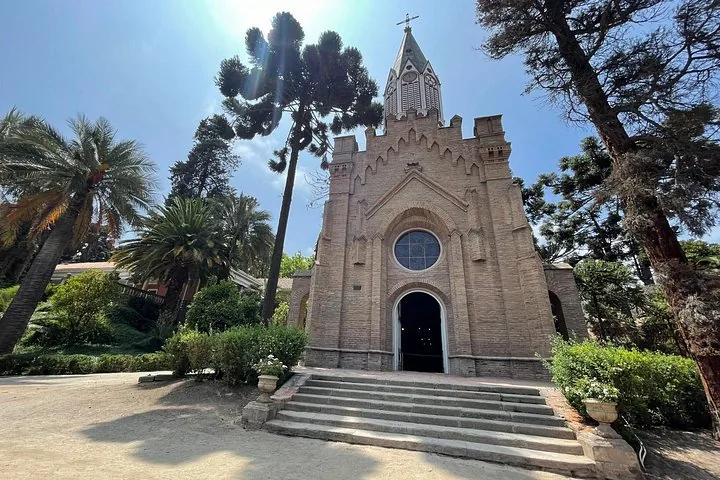 Brick chapel with a pointed spire among palms and araucaria trees