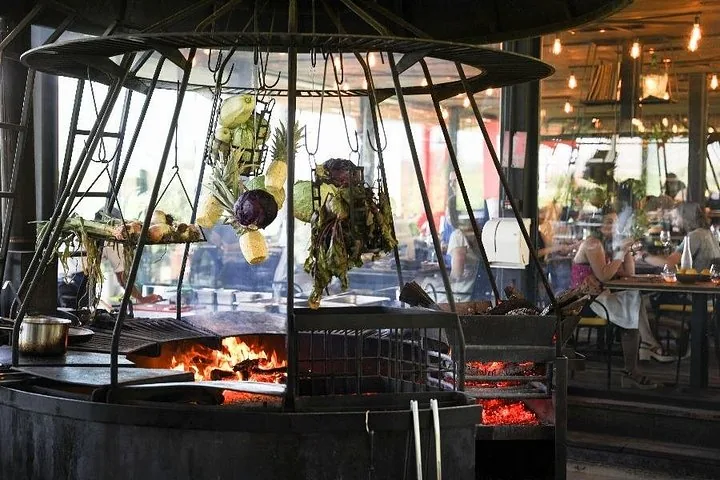 Open fire grill under a dome hung with pineapples and vegetables