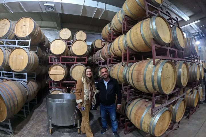 Two visitors posing between tall racks of stacked oak barrels